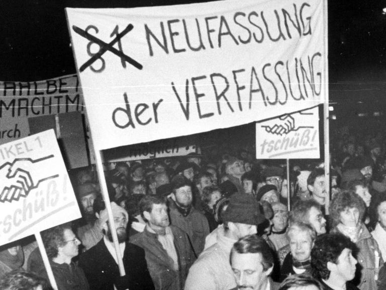 Montagsdemo in Dresden am 23. Oktober 1989. Menschen halten ein Banner mit dem Spruch "Neuverfassung der Verfassung" hoch.