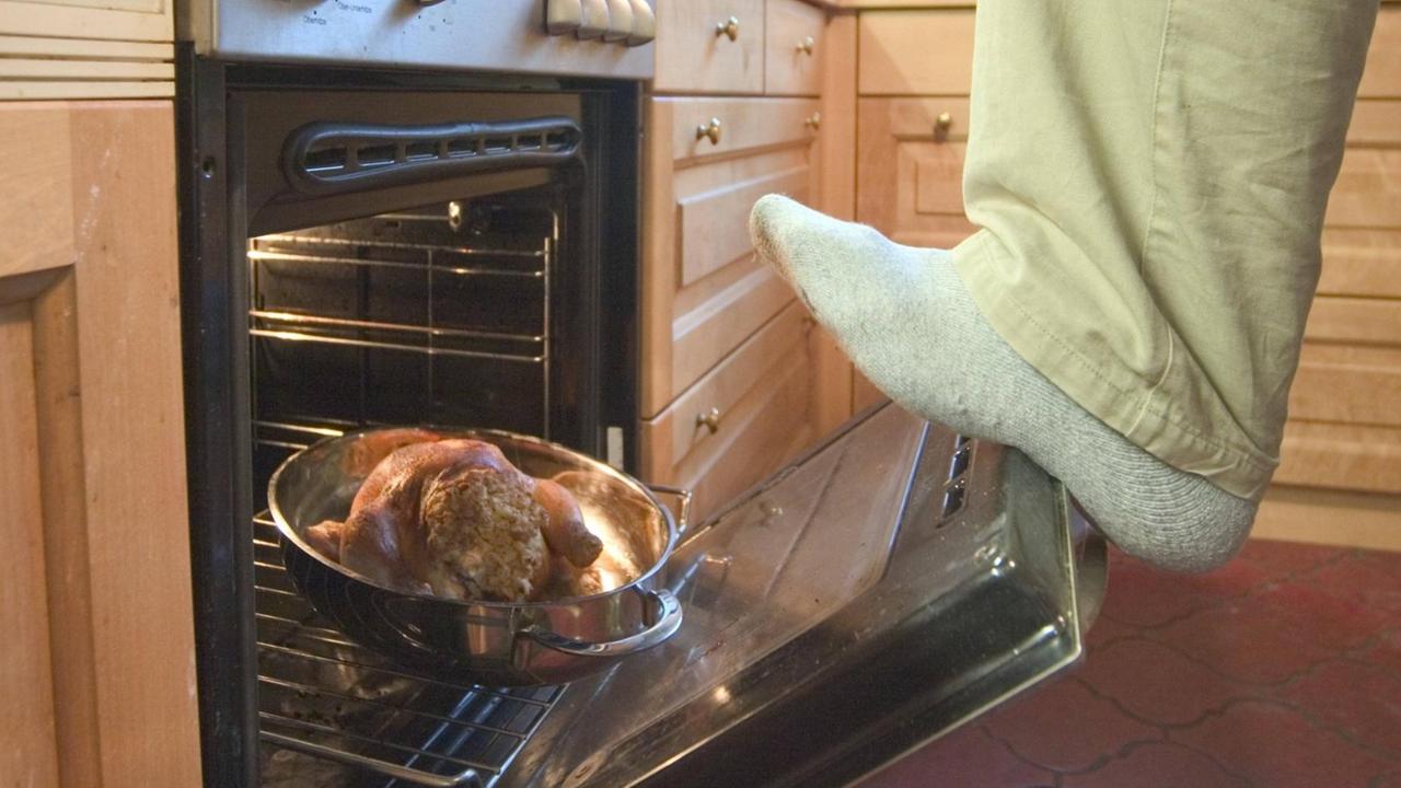 Ein Hosenbein mit Socke schubst schwungvoll ein Brathähnchen in einen Backofen. Ein Hosenbein mit Socke schubst schwungvoll ein Brathähnchen in einen Backofen.