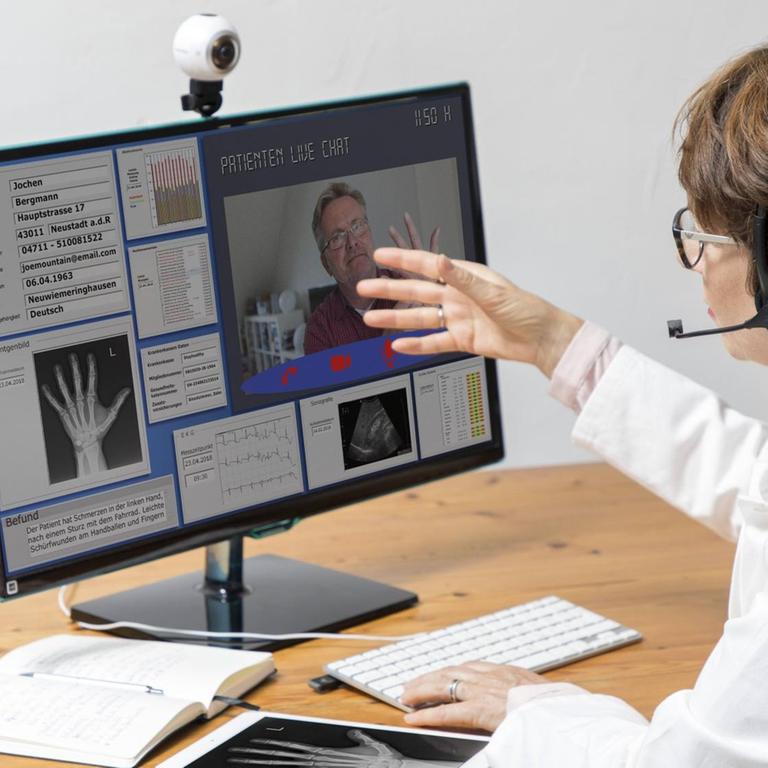 Symbolfoto zur Telemedizin, Ärztin in einer Praxis, kommuniziert mit dem Patienten über eine Webcam, Patientendaten und Befunde auf dem Monitor