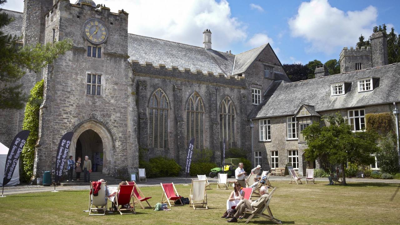 Menschen liegen in Liegestühlen vor dem gotischen Hauptgebäude von Dartington Hall. Menschen liegen in Liegestühlen vor dem gotischen Hauptgebäude von Dartington Hall.
