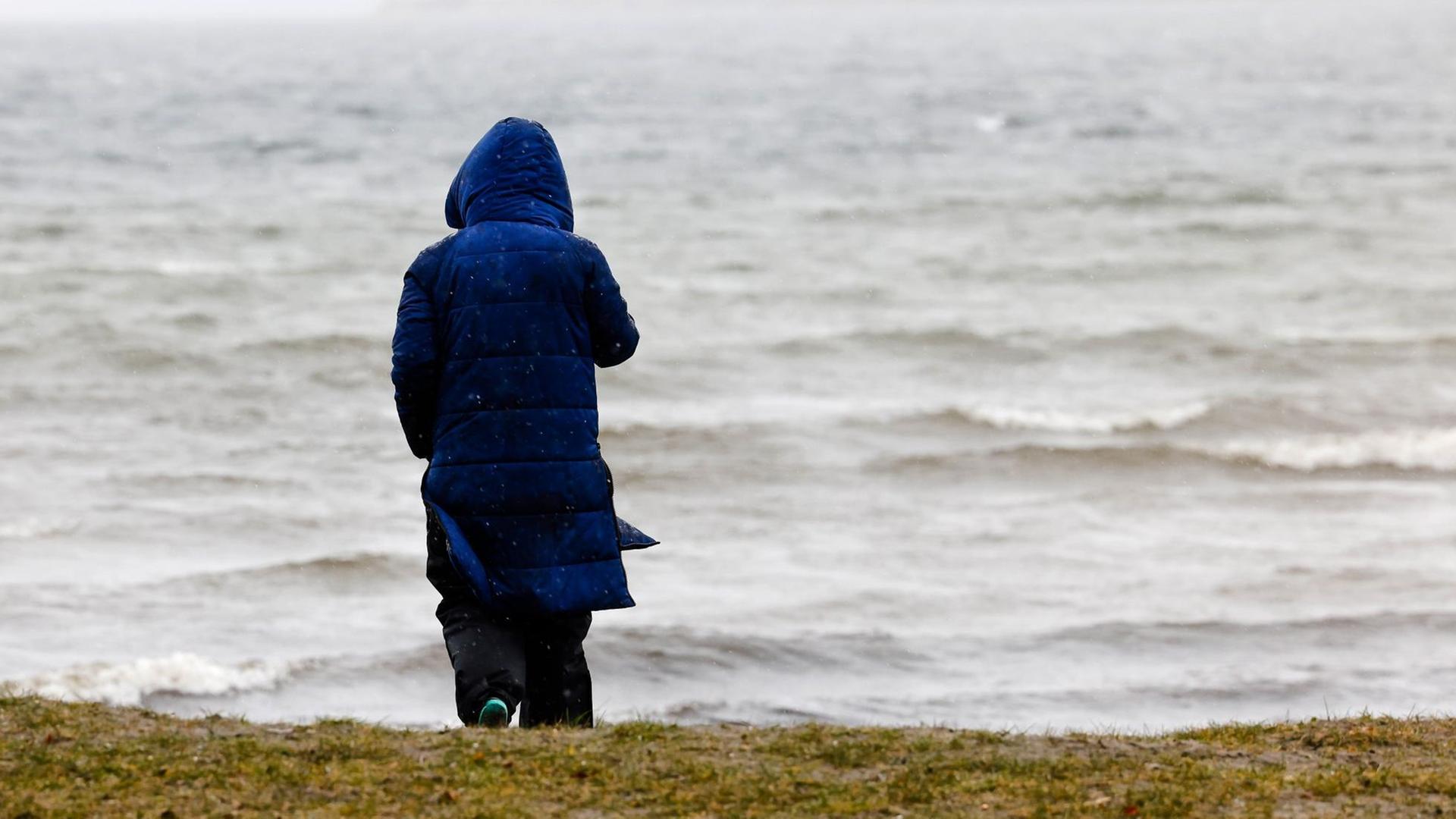 Eine Frau steht bei winterlichen Temperaturen und Regen an der Flensburger Förde.