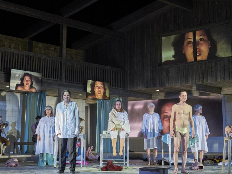 Szene aus dem Stück „Lärm. Blindes Sehen. Blinde sehen!“ am Schauspielhaus Hamburg. Eine Menschengruppe steht in OP-Kleidung auf der Bühne.