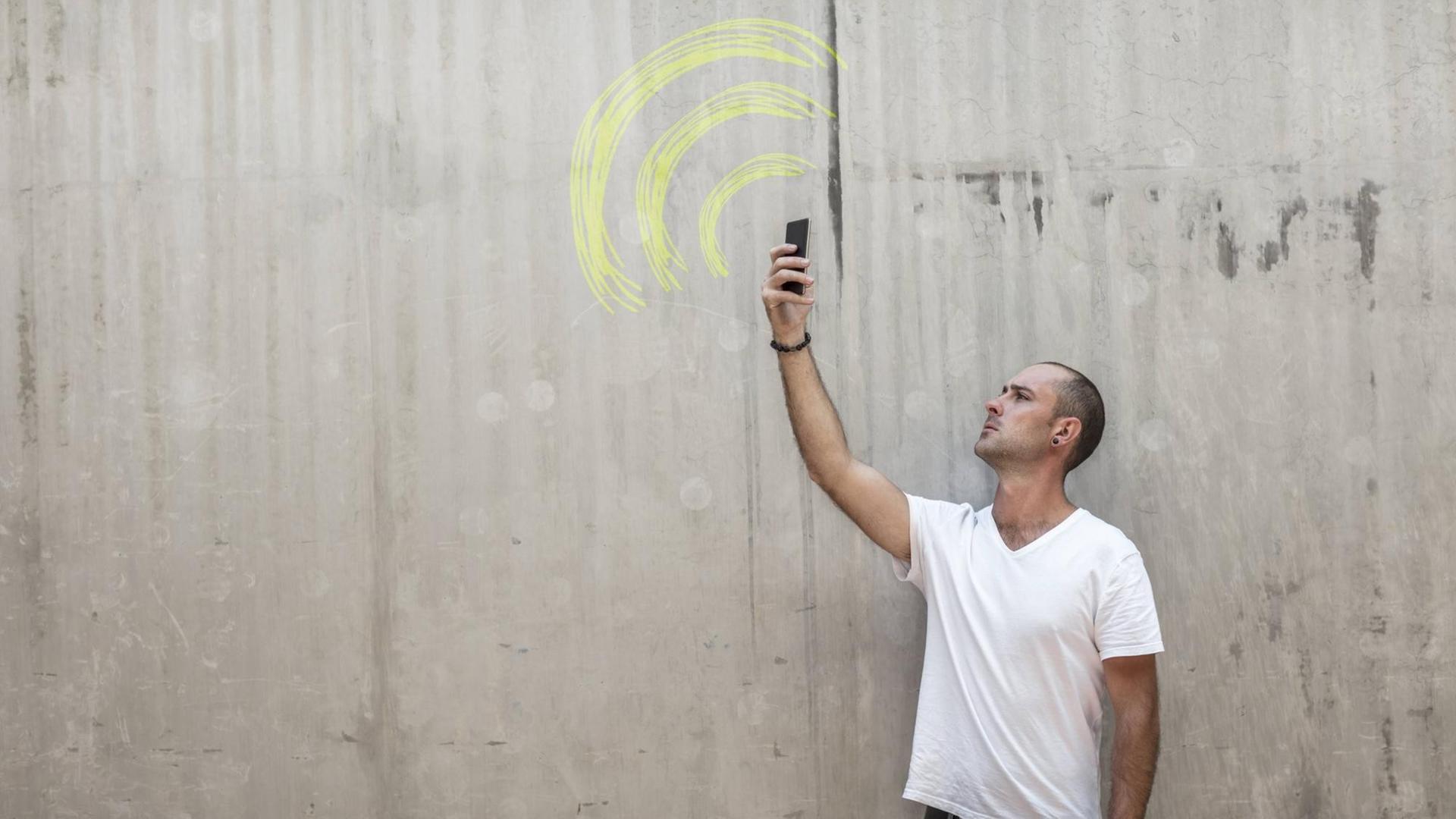 Mann hält sein Mobiltelefon in die Luft, auf einer Wand ist das WLAN Zeichen gemalt Mann hält sein Mobiltelefon in die Luft, auf einer Wand ist das WLAN Zeichen gemalt