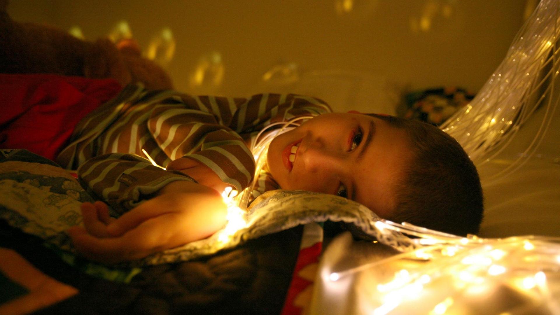 Ein Junge schaut im Liegen nach oben, sein Gesicht ist von einer Lichterkette erleuchtet.