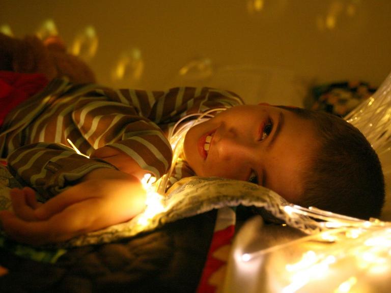 Ein Junge schaut im Liegen nach oben, sein Gesicht ist von einer Lichterkette erleuchtet.