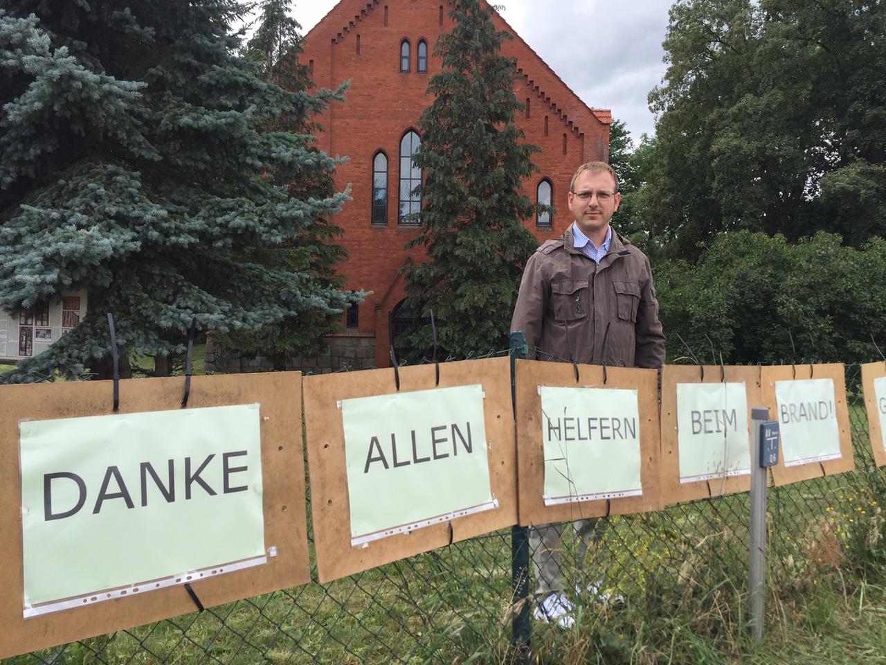 Ein Mann steht hinter einem Zaun. An dem Zaun hängen Plakate, die sich bei den Helfern bedanken Ein Mann steht hinter einem Zaun. An dem Zaun hängen Plakate, die sich bei den Helfern bedanken