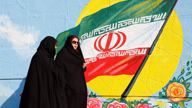 Zwei iranische Frauen in Teheran vor einer iranischen Flagge, die als Graffiti an eine Wand gesprüht ist