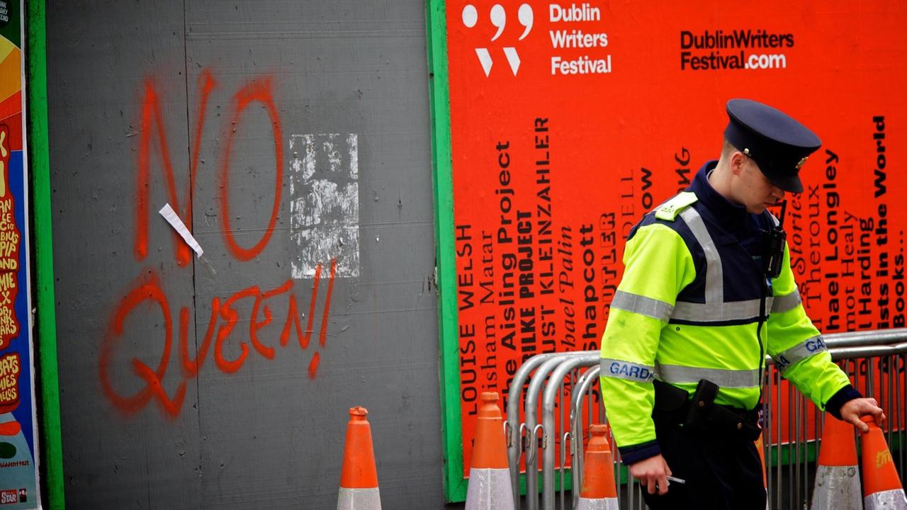 Ein Polizeibeamter steht am 15. Mai 2011 vor dem historischen Besuch der britischen Königin Elizabeth II. im Zentrum von Dublin, Irland, in der Nähe einer Mauer mit Graffiti mit der Aufschrift "No Queen" Der viertägige Besuch wurde am 17. Mai inmitten einer massiven Sicherheitsoperation beginnen. Eine  zuvor  durchgeführte Umfrage ergab, dass 77 Prozent der Iren den Besuch der Königin und von Prinz Philip begrüßen.