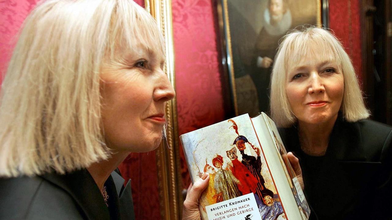 Die Schriftstellerin Brigitte Kronauer steht mit ihrem Buch vor einem Spiegel und blick uns aus diesem lächelnd entgegen. Sie erhielt 2005 in Darmstadt den Georg-Büchner-Preis. Die Schriftstellerin Brigitte Kronauer steht mit ihrem Buch vor einem Spiegel und blick uns aus diesem lächelnd entgegen. Sie erhielt 2005 in Darmstadt den Georg-Büchner-Preis.