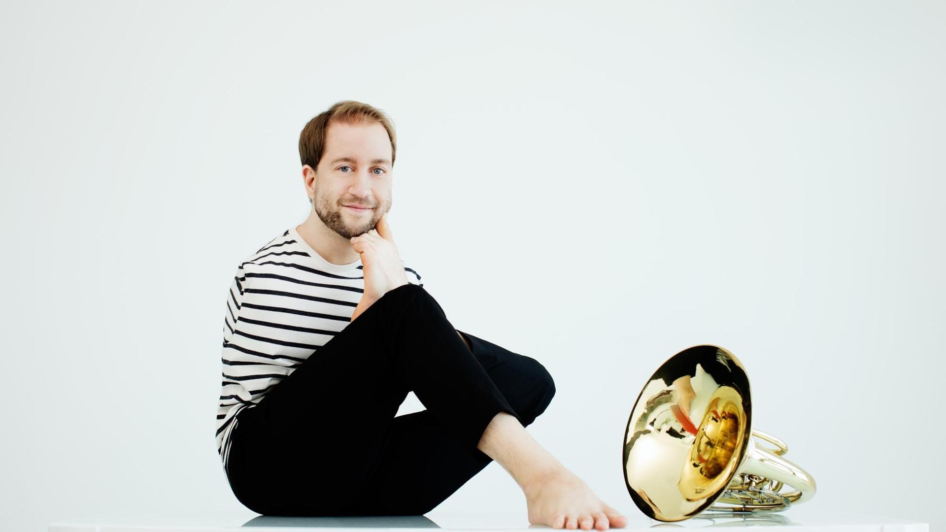 Ein junger Musiker sitzt auf dem Boden neben seinem Intstrument, dem Horn. Ein junger Musiker sitzt auf dem Boden neben seinem Intstrument, dem Horn.
