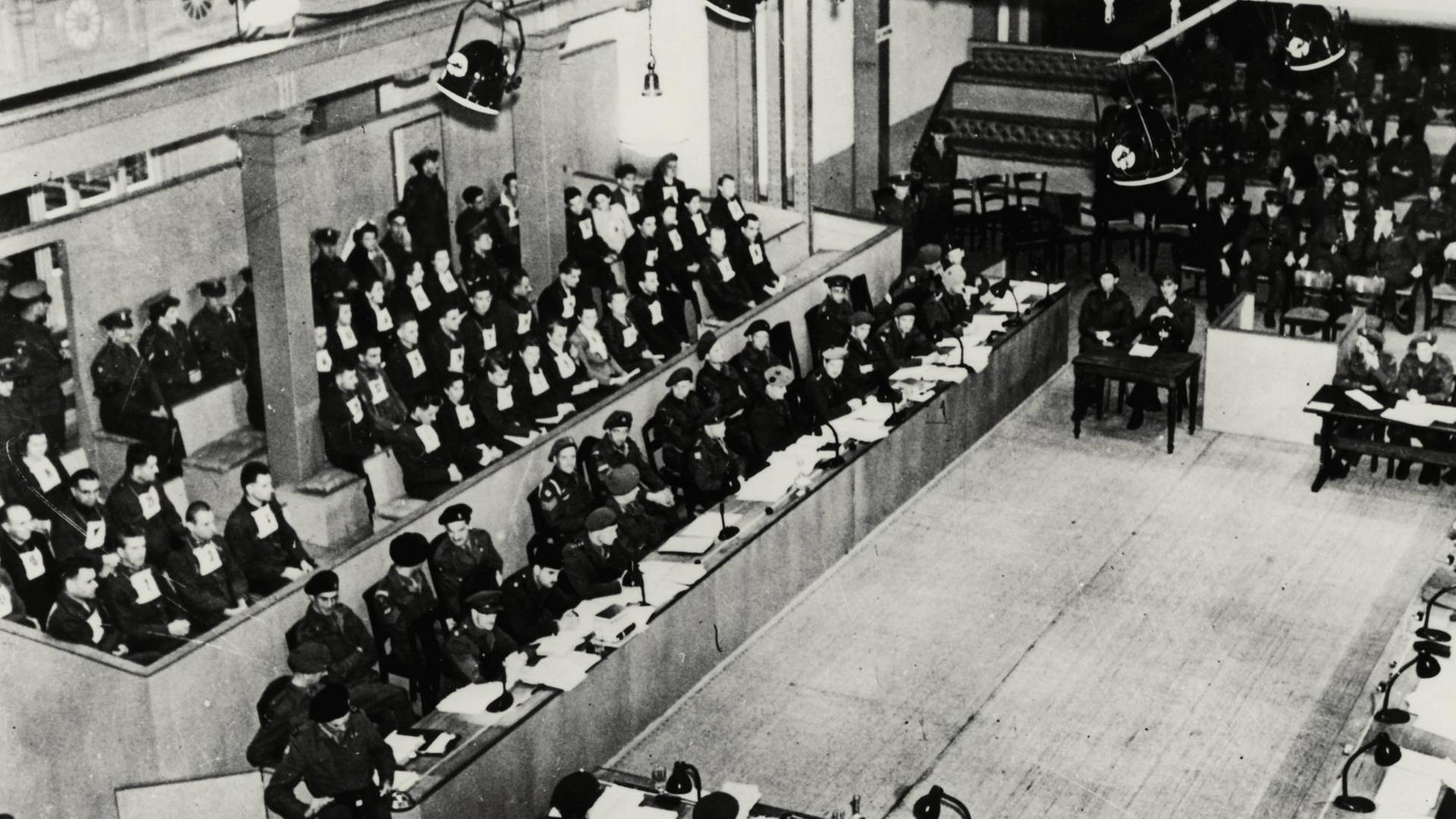 Prozess gegen die Wachmannschaft des Konzentrationslagers Bergen-Belsen vor einem britischen Militärgericht in Lüneburg, 16.9.1945 bis zur Urteilsverkündung am 20.11.1945. Blick in den Gerichtssaal während der Verfahrenseröffnung: Links die Anklagebank, davor die Verteidiger und die Anvertreter (Vordergrund). Foto, 16.9.1945 | In einer ehemaligen Turnhalle in Lüneburg richtete 1945 ein britisches Militär-Tribunal über die Verbrechen im KZ-Bergen-Belsen. Vorn links die angeklagte ehemalige SS-Wachmannschaft Prozess gegen die Wachmannschaft des Konzentrationslagers Bergen-Belsen vor einem britischen Militärgericht in Lüneburg, 16.9.1945 bis zur Urteilsverkündung am 20.11.1945. Blick in den Gerichtssaal während der Verfahrenseröffnung: Links die Anklagebank, davor die Verteidiger und die Anvertreter (Vordergrund). Foto, 16.9.1945 | In einer ehemaligen Turnhalle in Lüneburg richtete 1945 ein britisches Militär-Tribunal über die Verbrechen im KZ-Bergen-Belsen. Vorn links die angeklagte ehemalige SS-Wachmannschaft
