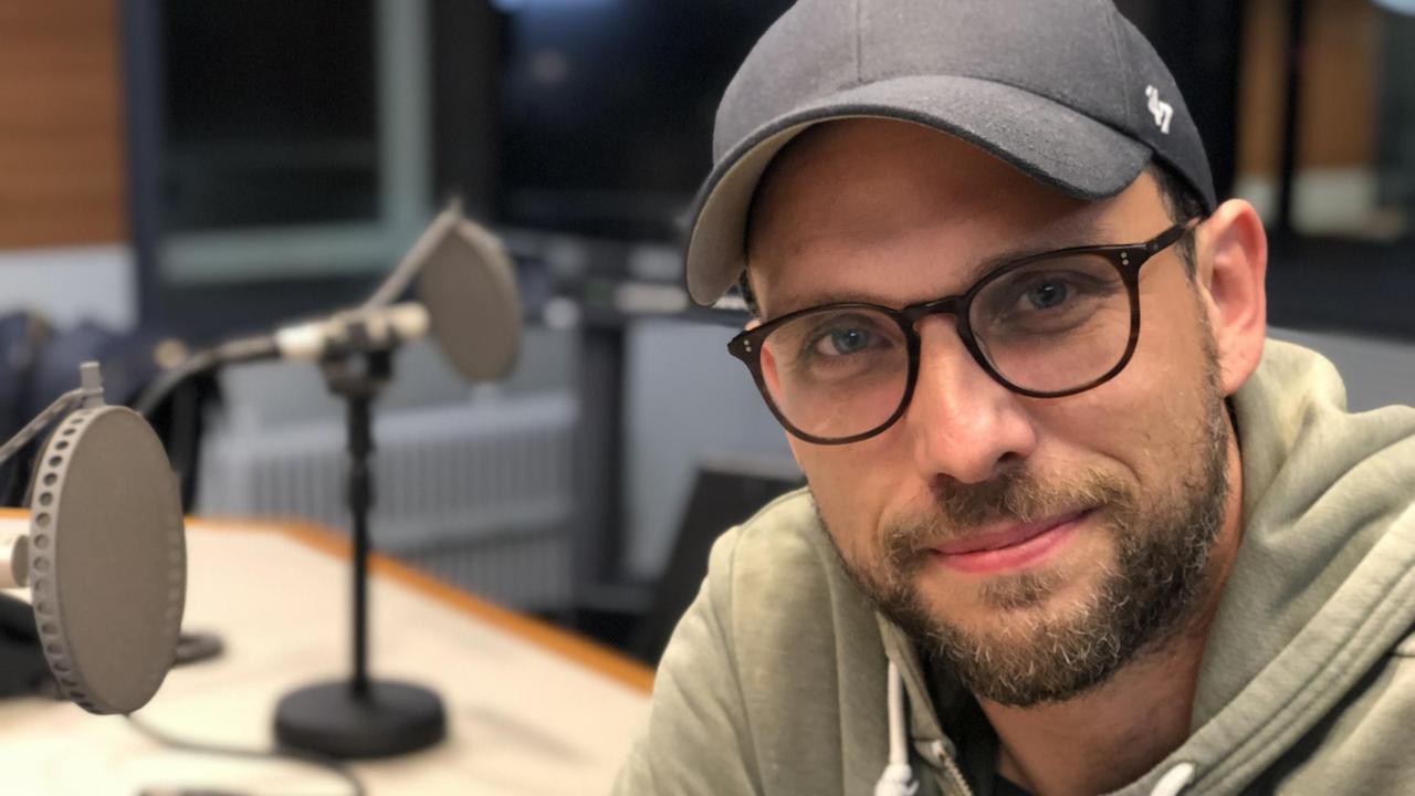 Ein junger Mann mit Brille und Basecap schaut lächelnd in die Kamera. Ein junger Mann mit Brille und Basecap schaut lächelnd in die Kamera.
