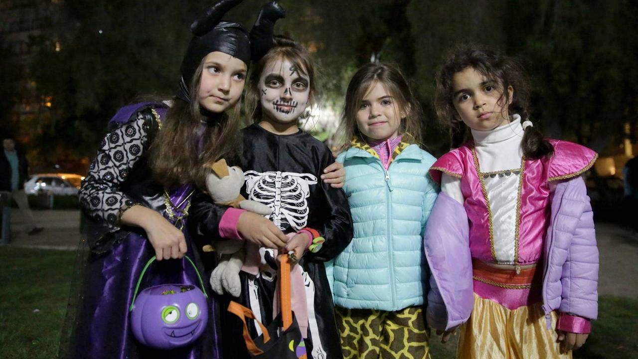 Kinder ziehen an Halloween abends im Dunkeln über die Straße, vier Kinder stehen nebeneinander verkleidet auf der Straße. Kinder ziehen an Halloween abends im Dunkeln über die Straße, vier Kinder stehen nebeneinander verkleidet auf der Straße.