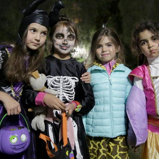 Kinder ziehen an Halloween abends im Dunkeln über die Straße, vier Kinder stehen nebeneinander verkleidet auf der Straße.