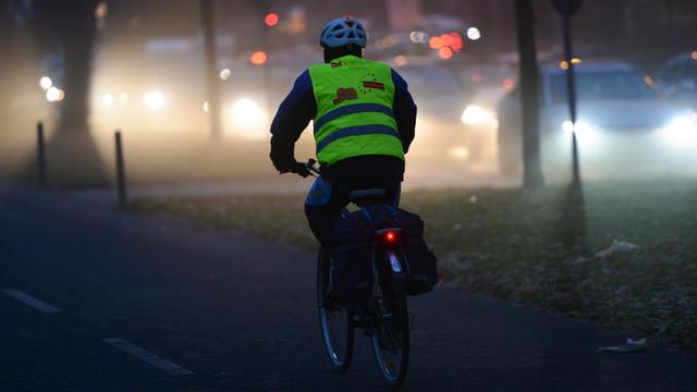 Ein Fahrradfahrer fährt im Dunkeln auf einer Straße, er trägt eine gelbe Warnweste.
