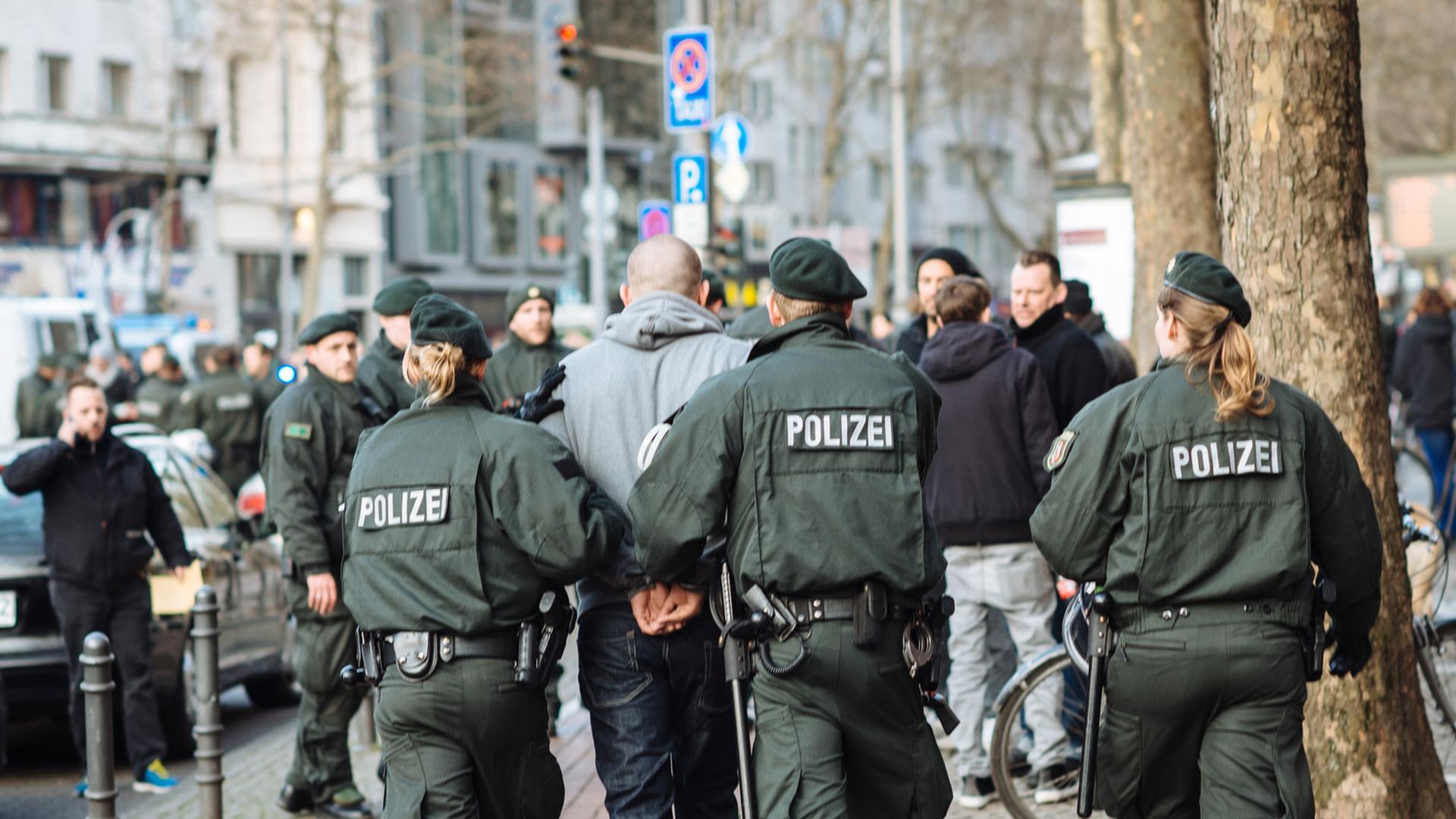 Polizisten führen nach einer Massenschlägerei unter Fußballfans in Köln eine verhaftete Person ab. Polizisten führen nach einer Massenschlägerei unter Fußballfans in Köln eine verhaftete Person ab.