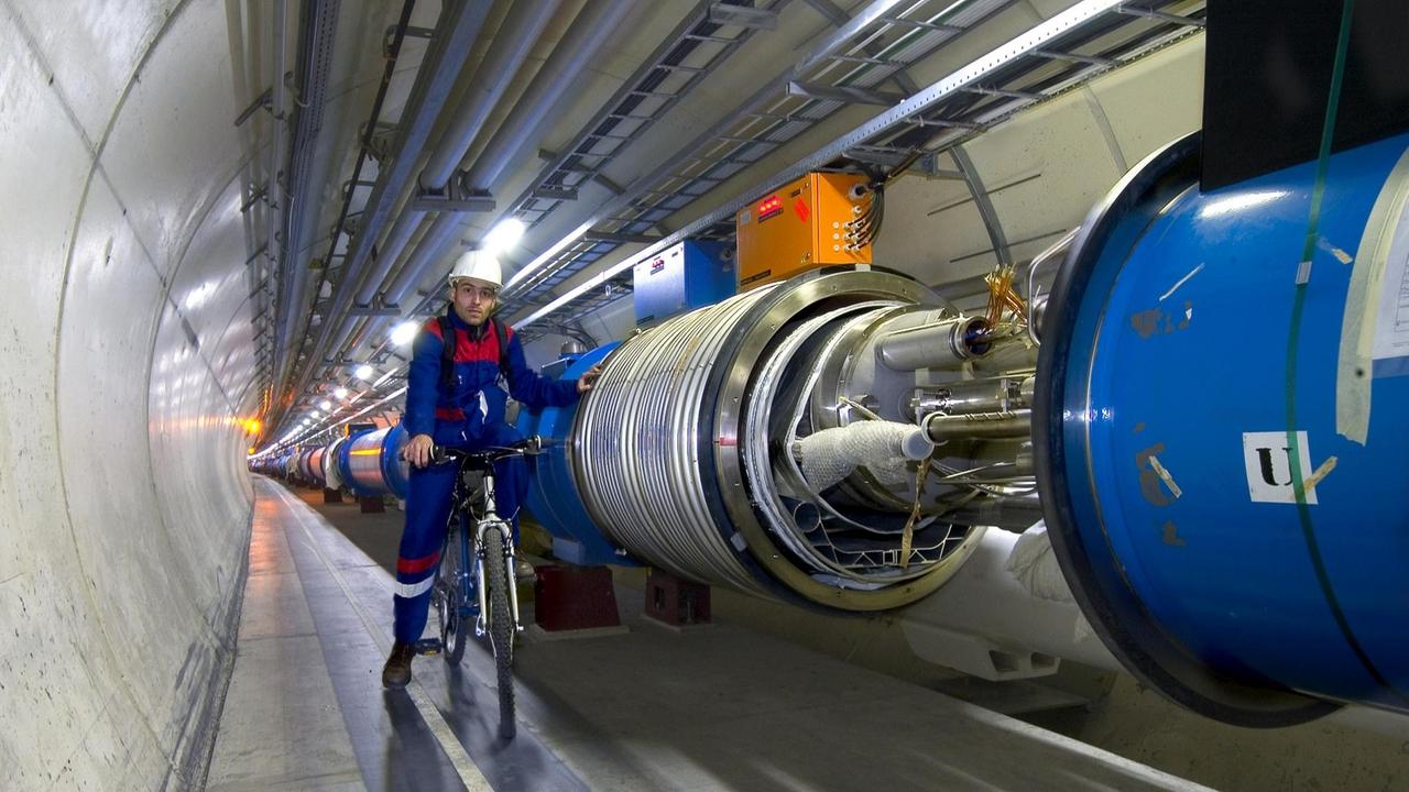 Ein CERN-Mitarbeiter im blauen Overall sitzt auf einem Fahrrad in der Tunnelröhre des LHC-Teilchenbeschleunigers