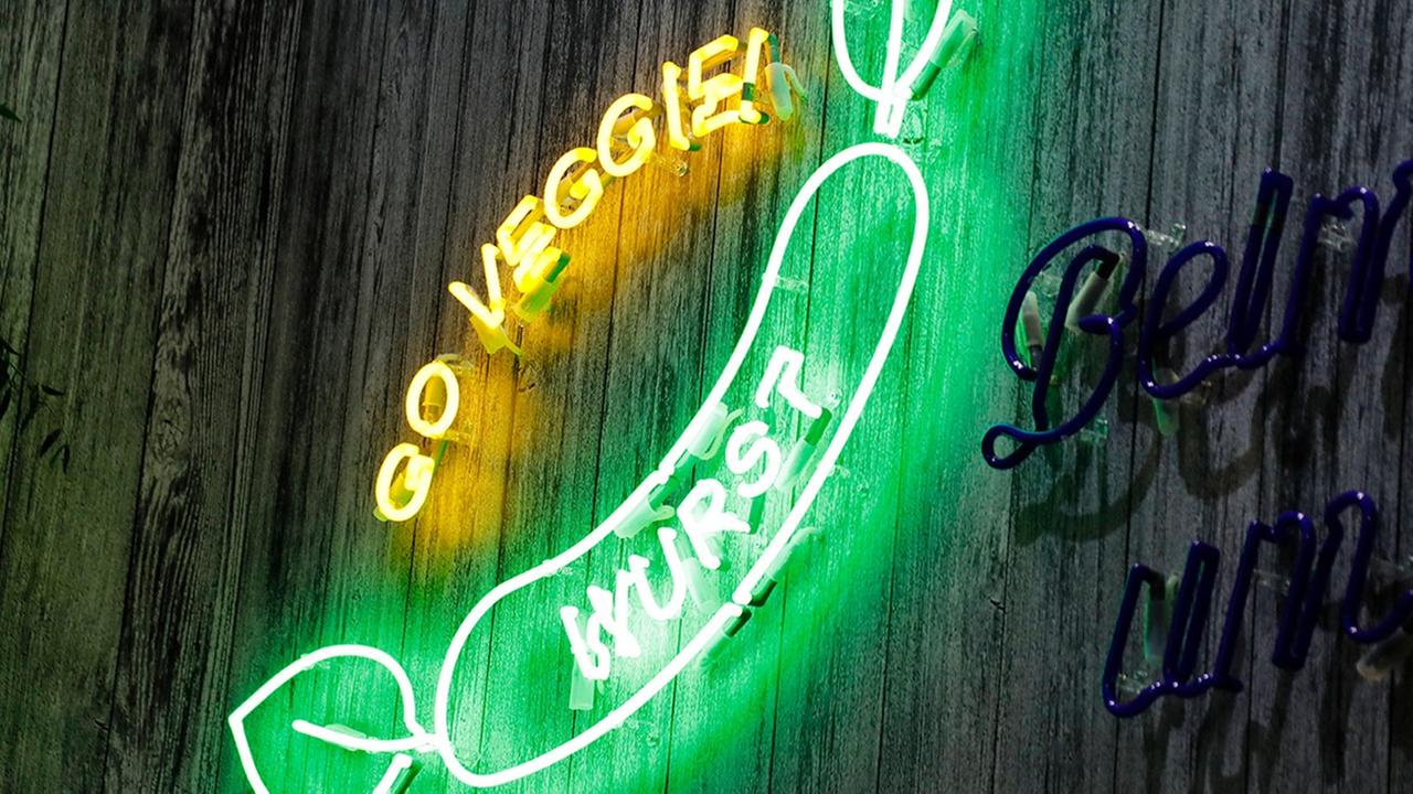 Eine Leuchtreklame mit einer grünen Wurst, die an den Enden jeweils Blätter hat. Daneben steht "Go Veggie".