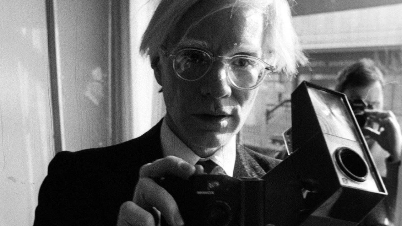 Porträt von Andy Warhol mit seiner Kamera in der Hand.