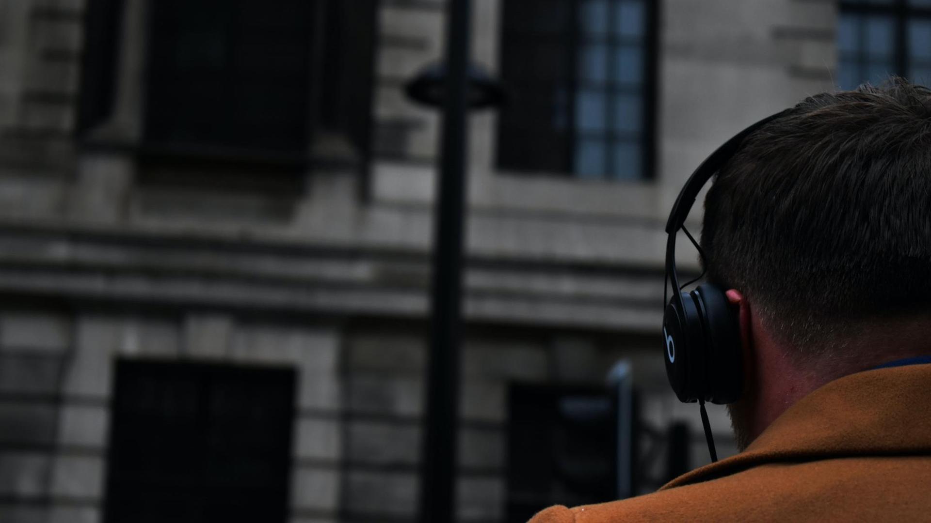 Das Bild zeigt einen Mann von hinten mit Kopfhörern auf einer Straße. Nachrichtenpodcasts sind beliebte Begleiter für Pendel- und Alltagswege.