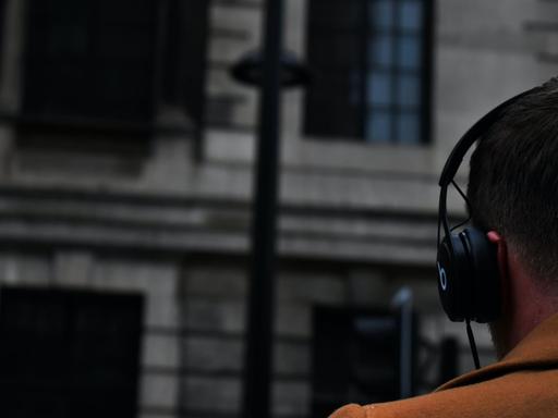 Das Bild zeigt einen Mann von hinten mit Kopfhörern auf einer Straße. Nachrichtenpodcasts sind beliebte Begleiter für Pendel- und Alltagswege.