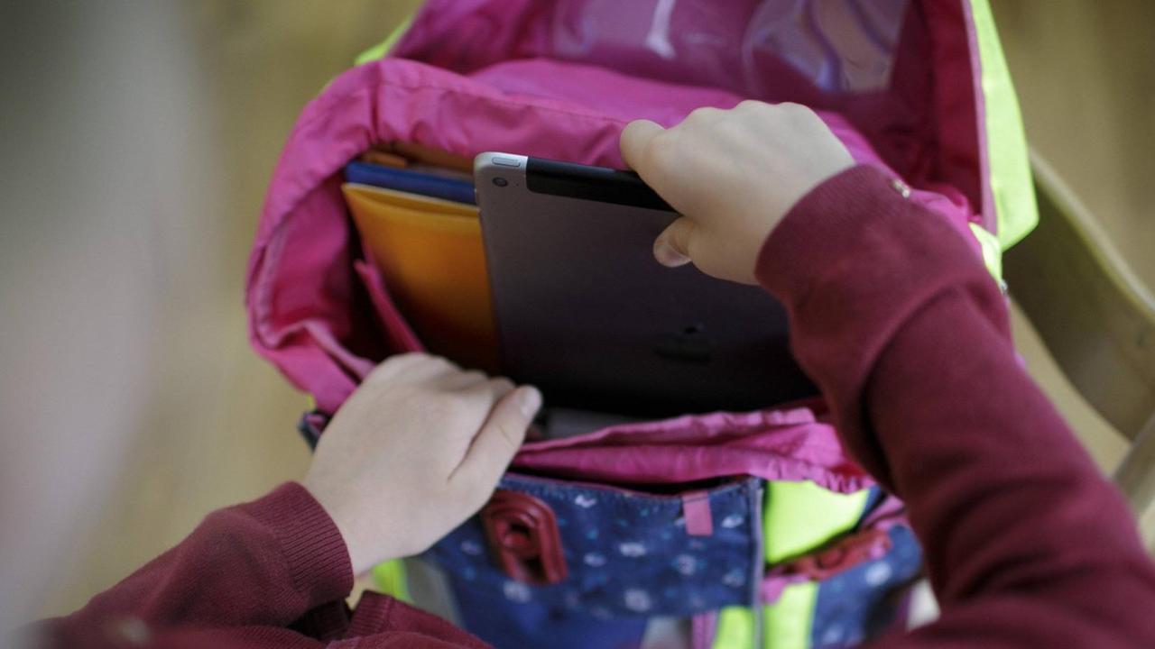 Ein Mädchen packt ein Tablet in ihren Schulranzen Ein Mädchen packt ein Tablet in ihren Schulranzen