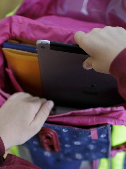 Ein Mädchen packt ein Tablet in ihren Schulranzen