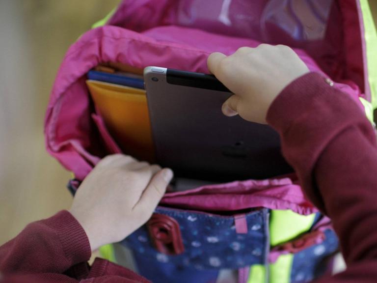 Ein Mädchen packt ein Tablet in ihren Schulranzen