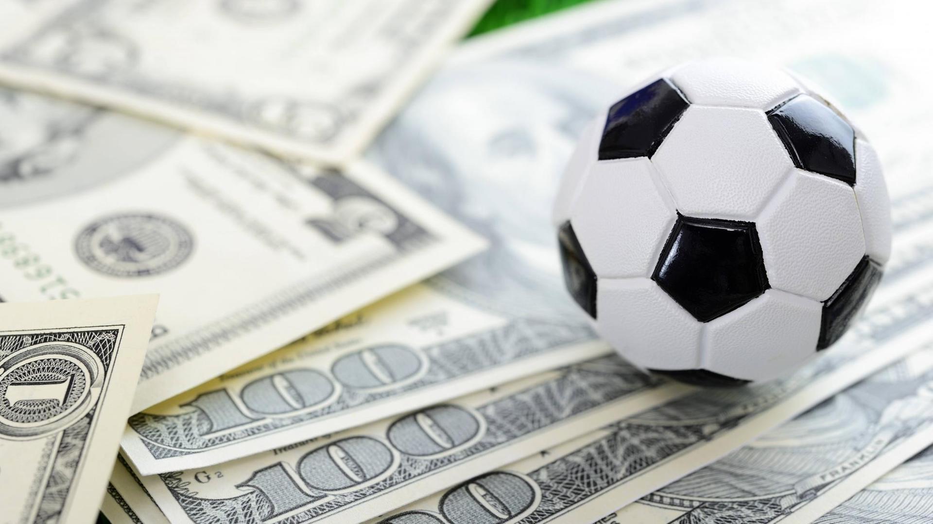 Ein Miniaturfußball liegt auf mehreren Dollar-Scheinen Ein Miniaturfußball liegt auf mehreren Dollar-Scheinen