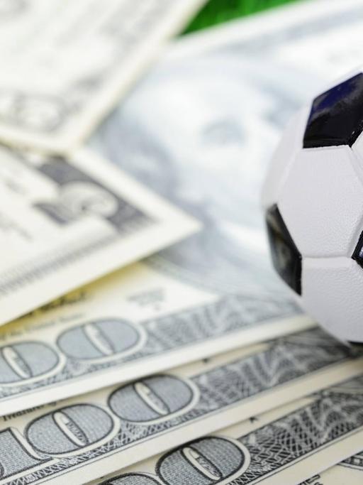 Ein Miniaturfußball liegt auf mehreren Dollar-Scheinen
