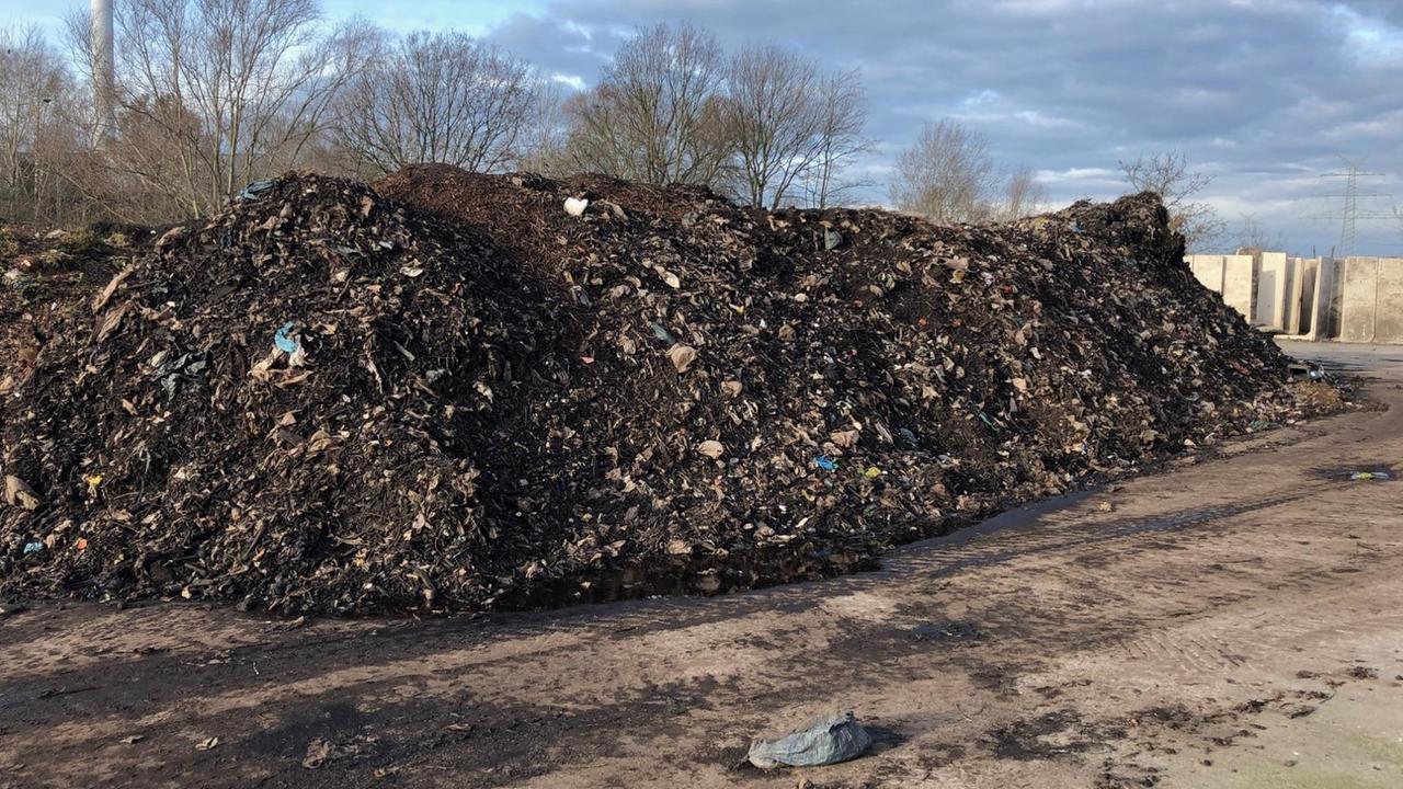 Ein beeindruckender schwarzbrauner Müllberg unter freiem Himmel mit Materialien, die im Biomüll nichts verloren haben.