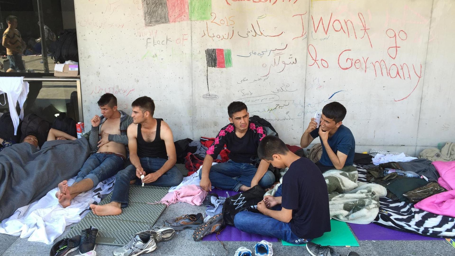 Geflüchtete junge Männer sitzen wir einer Wand, an der "I want go to Germany" geschrieben steht. Geflüchtete junge Männer sitzen wir einer Wand, an der "I want go to Germany" geschrieben steht.