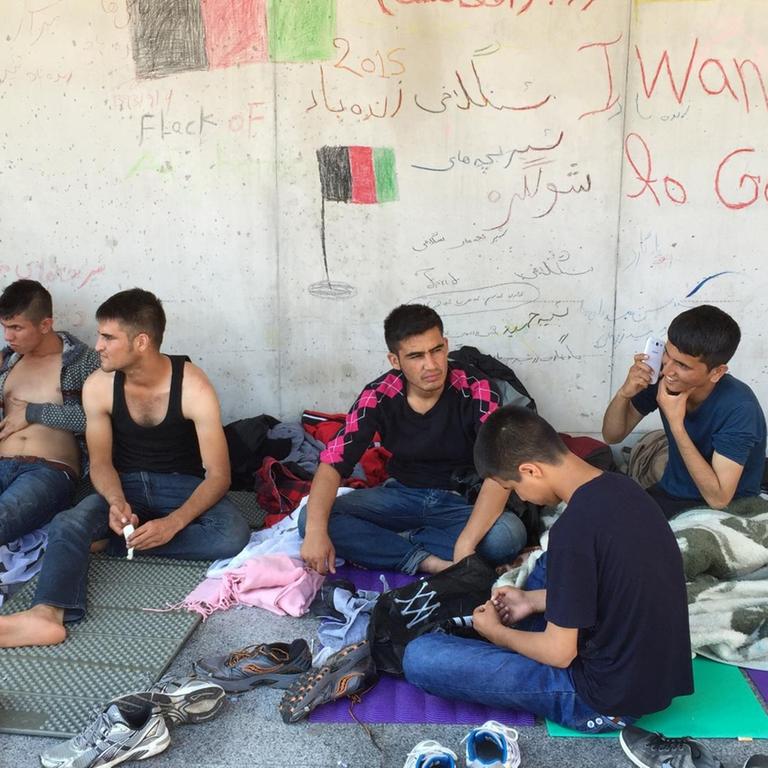 Geflüchtete junge Männer sitzen wir einer Wand, an der "I want go to Germany" geschrieben steht.