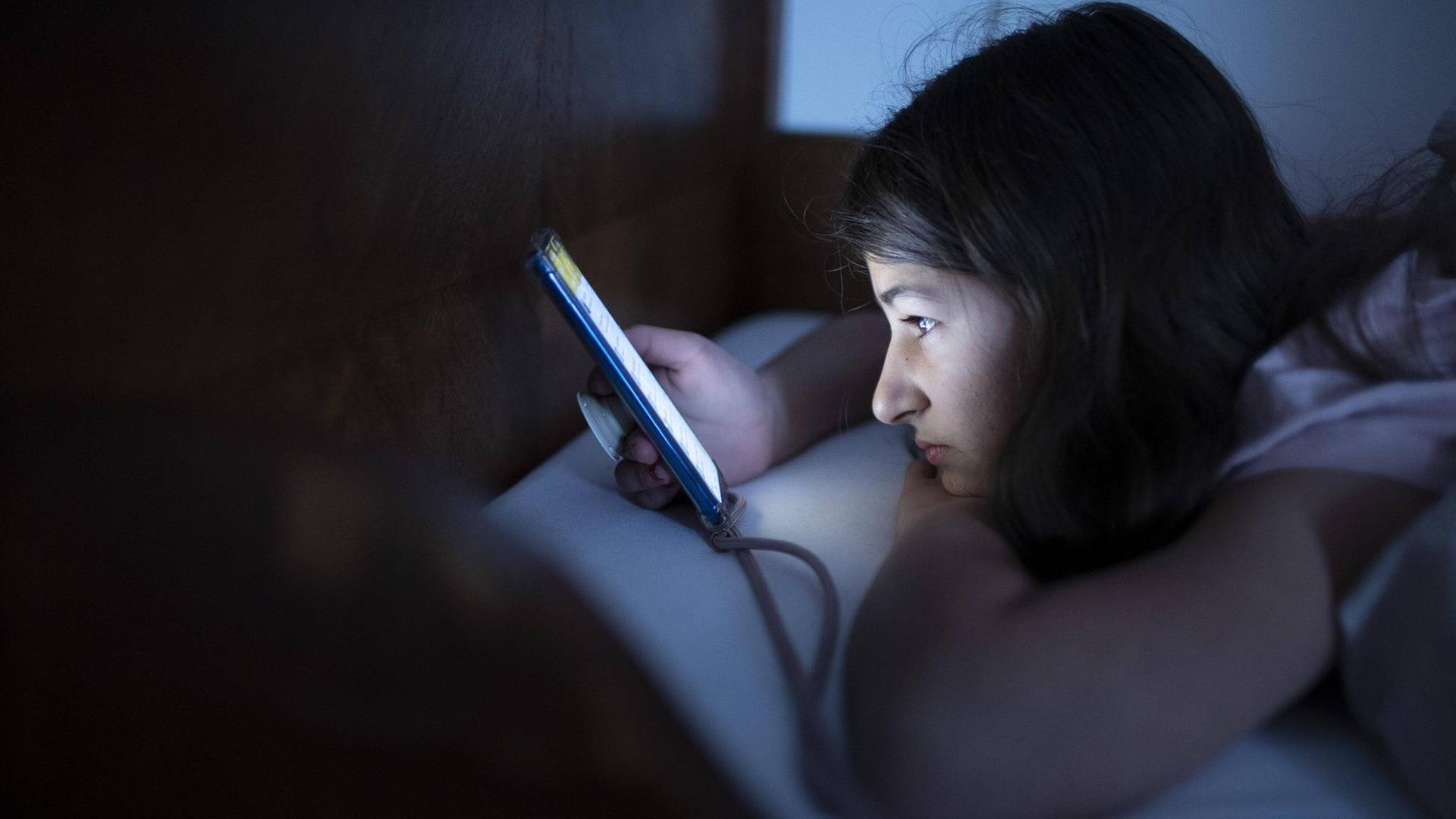 Ein Mädchen schaut im Bett auf sein Smartphone Ein Mädchen schaut im Bett auf sein Smartphone
