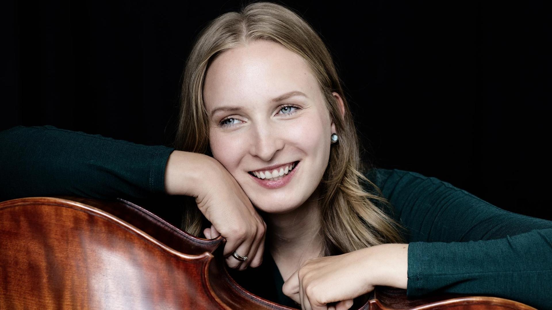 Die Cellistin Marie-Elisabeth Hecker ist im Halbporträt zu sehen, mit lächelndem Blick, die Arme aufs Cello gelehnt.