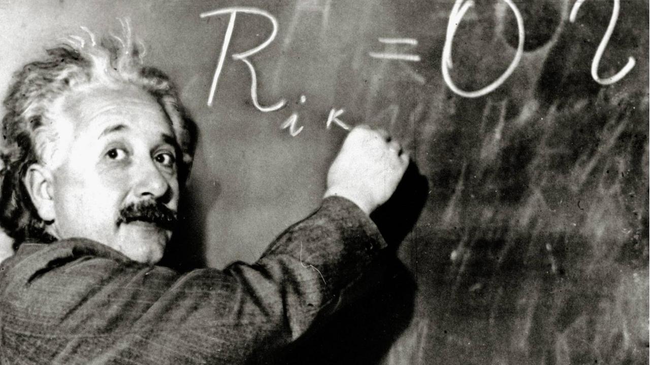 Albert Einstein schreibt eine Formel an die Tafel und guckt dabei in die Kamera. Albert Einstein schreibt eine Formel an die Tafel und guckt dabei in die Kamera.