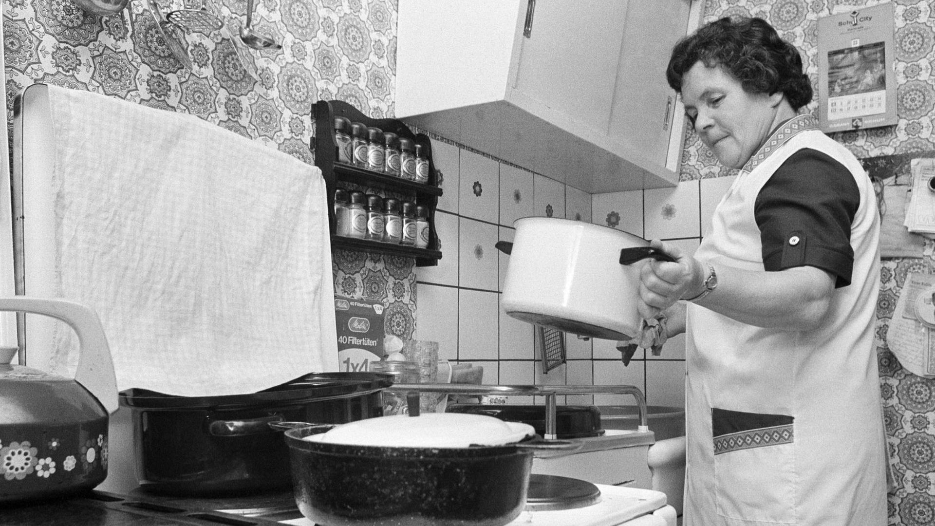 Eine ältere Frau bereitet an einem Herd das Essen zu - Deutschland in den 70ern. Eine ältere Frau bereitet an einem Herd das Essen zu - Deutschland in den 70ern.