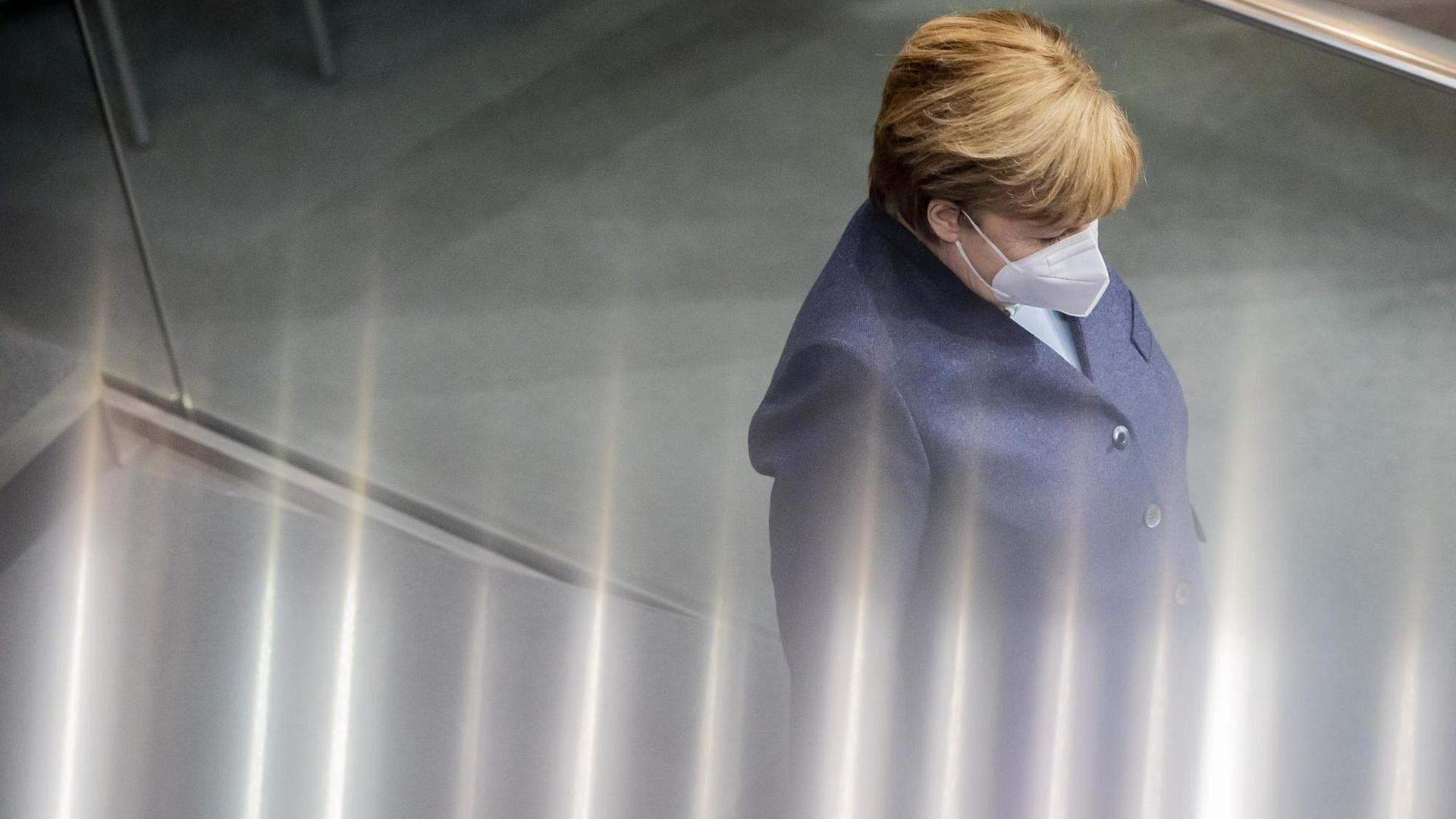 Angela Merkel trägt Maske und ist in einer Seitenansicht zu sehen. Vom unteren Rand treten irrisierende Lichteffeke ins Bild, die das Geschehen veruneindeutigen.