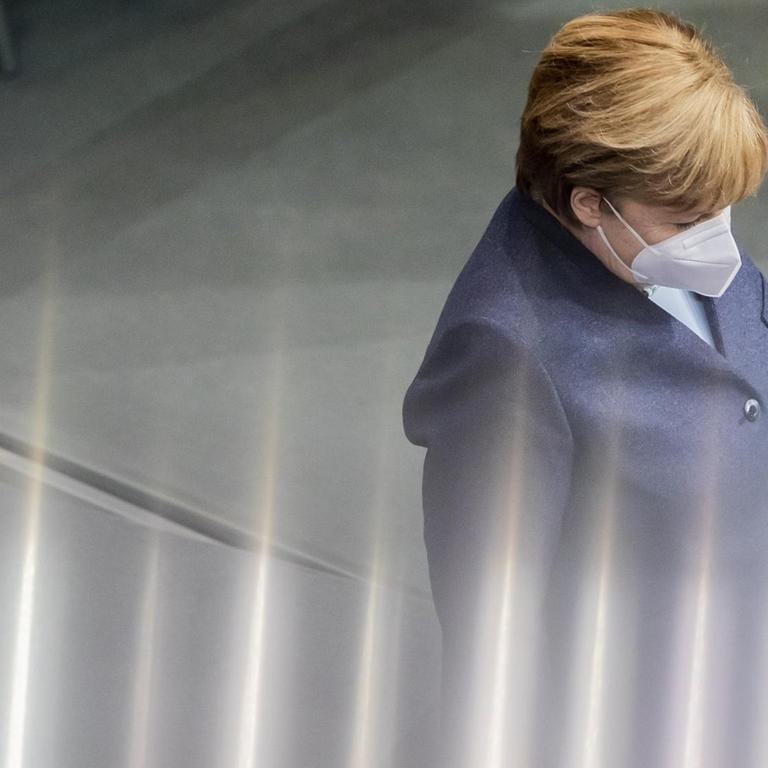 Angela Merkel trägt Maske und ist in einer Seitenansicht zu sehen. Vom unteren Rand treten irrisierende Lichteffeke ins Bild, die das Geschehen veruneindeutigen.
