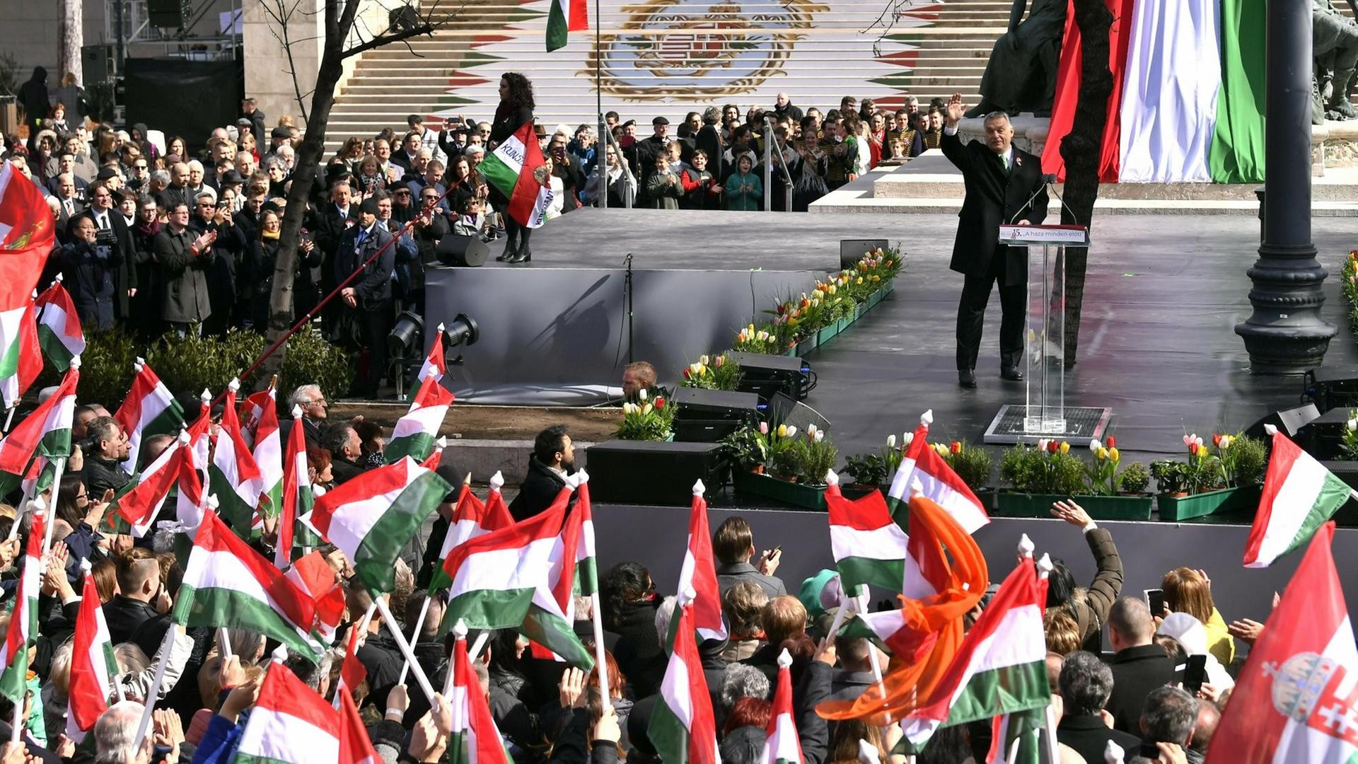 Das Bild zeigt Viktor Orban aus der Ferne. Er winkt Anhängern zu, die die ungarische Flaggen schwenken.