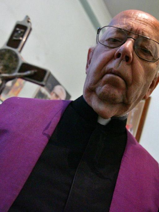 Ein Portrait von Pater Gabriele Amorth. In der rechten Hand hält er ein Kruzifix vor die Kamera.