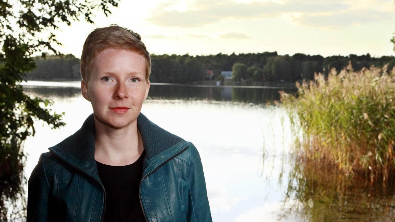 Die Autorin Judith Zander sitzt vor einem See und schaut in die Kamera. Die Autorin Judith Zander sitzt vor einem See und schaut in die Kamera.