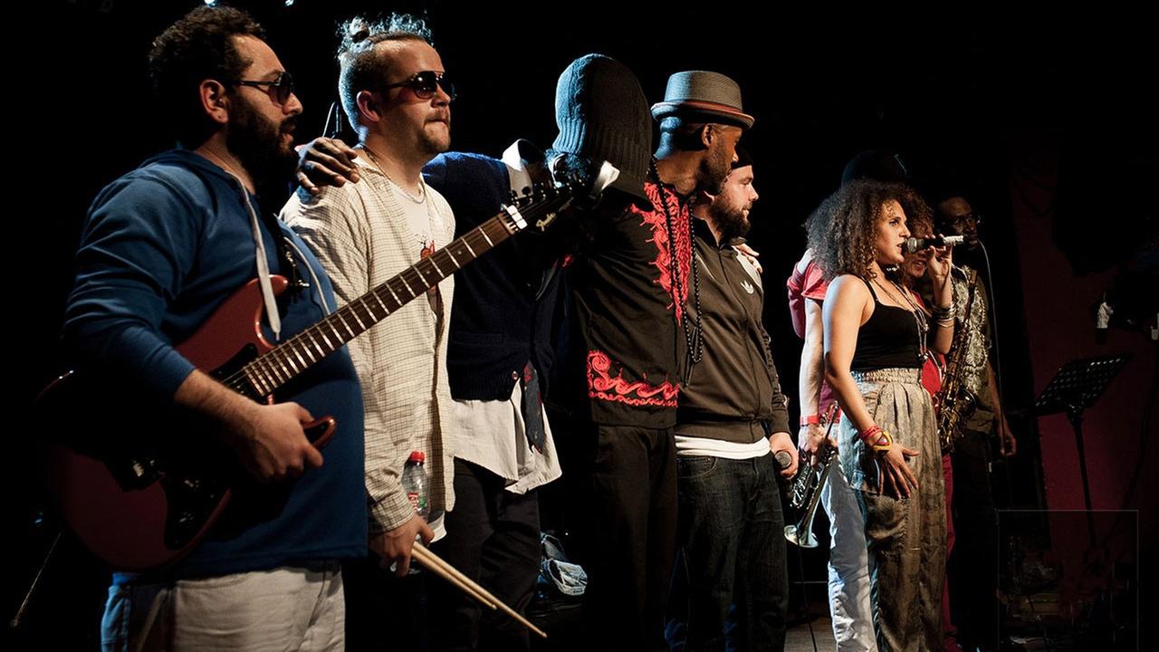 Acht Musiker der Hip Hop Band Nomadic Massive stehen auf einer Bühne und verabschieden sich beim Publikum Acht Musiker der Hip Hop Band Nomadic Massive stehen auf einer Bühne und verabschieden sich beim Publikum