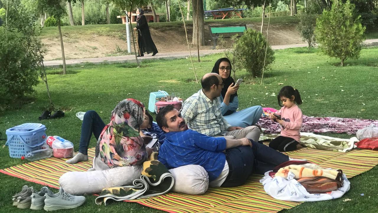 Eine Familie liegt und isst auf einer Matte in einem Park.