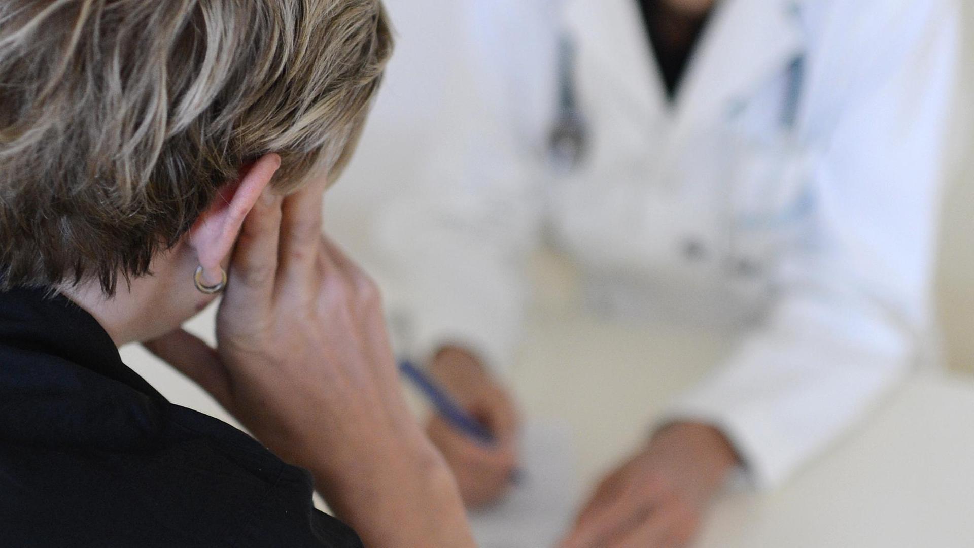 Eine Frau stützt ihren Kopf auf ihre Hand. Vor ihr eine freundliche Ärztin die sich Notizen macht.