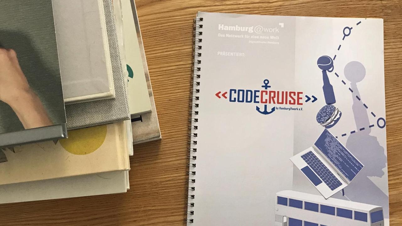 Eine hellblau-graue Mappe im modischen Design liegt auf einem Holztisch, daneben diverse weitere Broschüren Eine hellblau-graue Mappe im modischen Design liegt auf einem Holztisch, daneben diverse weitere Broschüren