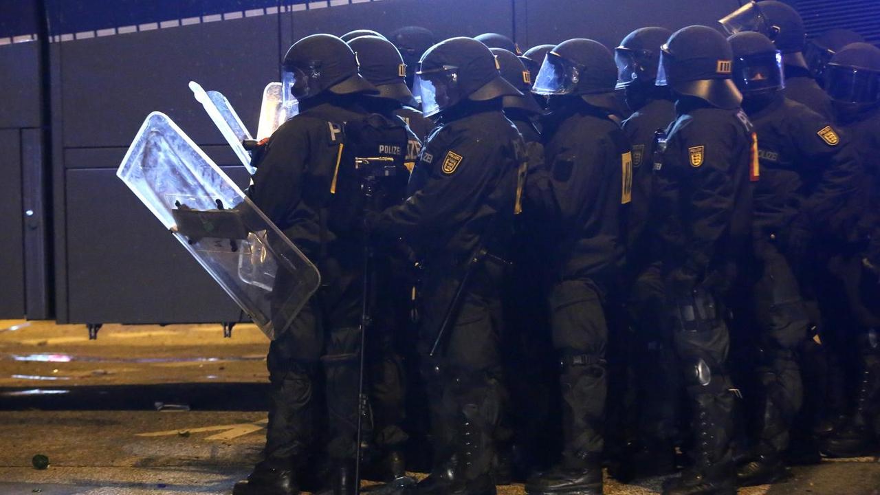 Die Gruppe von Polizisten steht im Dunkeln in voller Kampfmonitur mit Schildern neben einem Wasserwerfer. Die Gruppe von Polizisten steht im Dunkeln in voller Kampfmonitur mit Schildern neben einem Wasserwerfer.