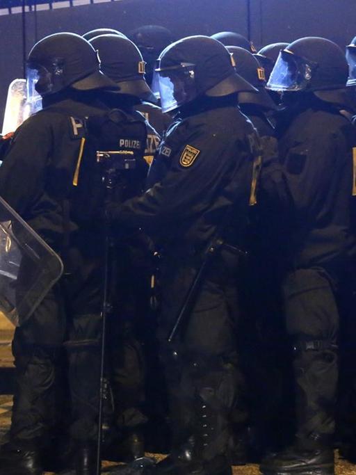 Die Gruppe von Polizisten steht im Dunkeln in voller Kampfmonitur mit Schildern neben einem Wasserwerfer.