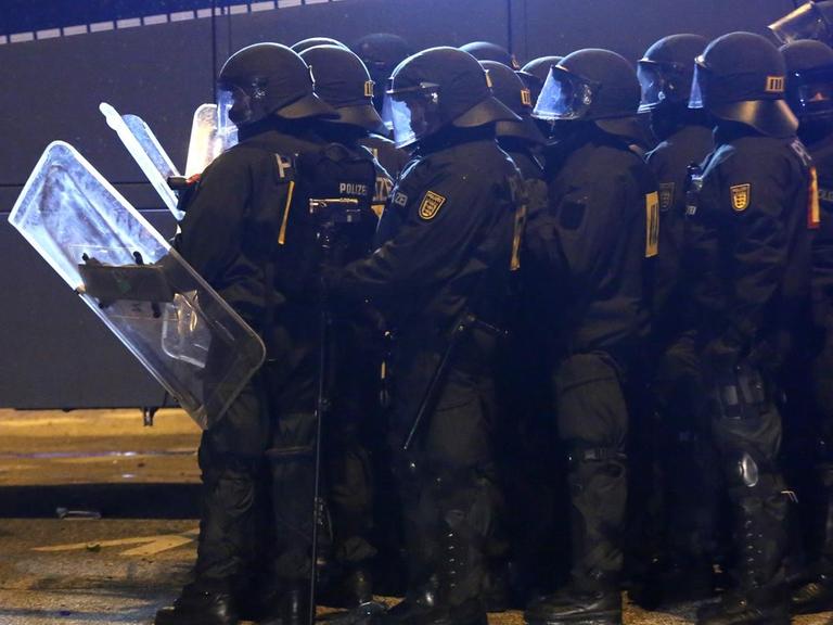 Die Gruppe von Polizisten steht im Dunkeln in voller Kampfmonitur mit Schildern neben einem Wasserwerfer.