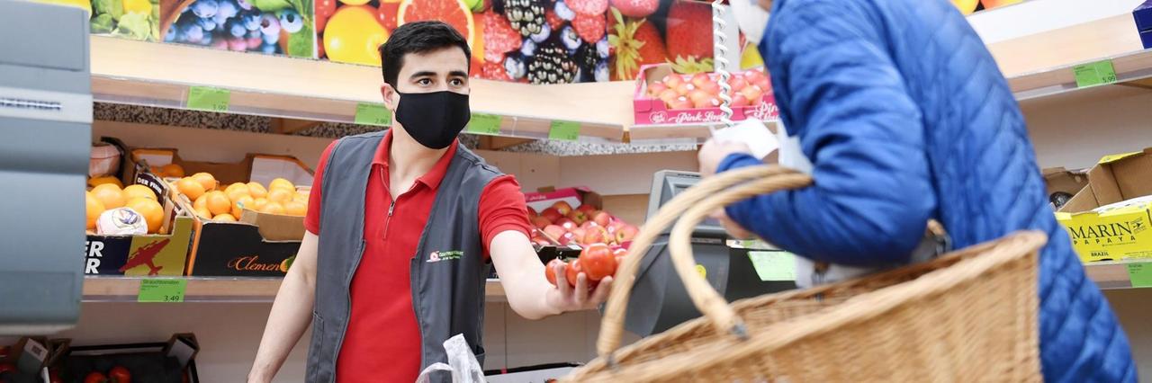 22.04.2020, Bayern, Rosenheim: Ein Mitarbeiter eines Lebensmittelgeschäfts bedient in der Gemüseabteilung eine Kundin und trägt eine Maske als Mund- und Nasenschutz. 22.04.2020, Bayern, Rosenheim: Ein Mitarbeiter eines Lebensmittelgeschäfts bedient in der Gemüseabteilung eine Kundin und trägt eine Maske als Mund- und Nasenschutz.